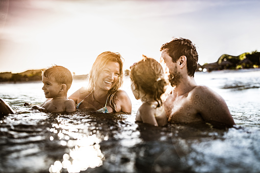 Young happy family talking while enjoying in sea at sunset. Copy space.