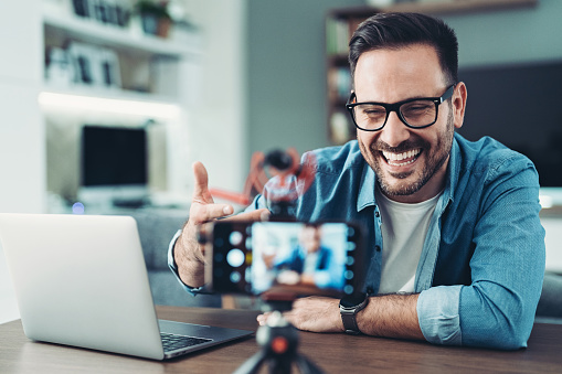Smiling man using cell phone to film a video in the living room