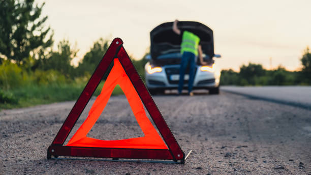 istock Broken silver luxury car emergency accident. Man driver installing red triangle stop sign on road. Sport automobile turned on blinkers technical problems on the road. Safety procedure vehicle broken down 1939284666