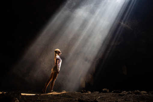 Happy woman standing in the cave and looking at sunlight entering. Copy space.