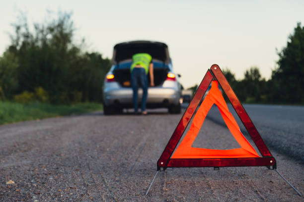 istock Unrecognizable sad driver in reflective vest. Male driver standing near broken car with open up hood. Red triangle to warn other road users of car breakdown or engine failure stop at countryside highway. Emergency traffic 1939285722
