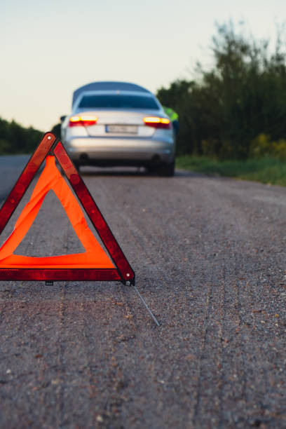istock Broken silver luxury car emergency accident. Man driver installing red triangle stop sign on road. Sport automobile turned on blinkers technical problems on the road. Safety procedure vehicle broken down 1939286792