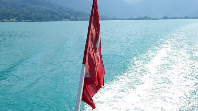 Swiss Flag Waving with Sunlight on Passenger Ship and Mountain on Lake Brienz in a Sunny Summer Day