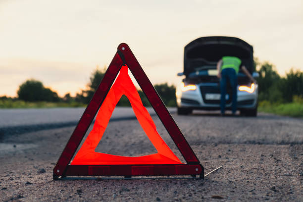istock Unrecognizable sad driver in reflective vest. Male driver standing near broken car with open up hood. Red triangle to warn other road users of car breakdown or engine failure stop at countryside highway. Emergency traffic 1939287849