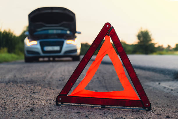 istock Broken silver luxury car emergency accident. Man driver installing red triangle stop sign on road. Sport automobile turned on blinkers technical problems on the road. Safety procedure vehicle broken down 1939288939