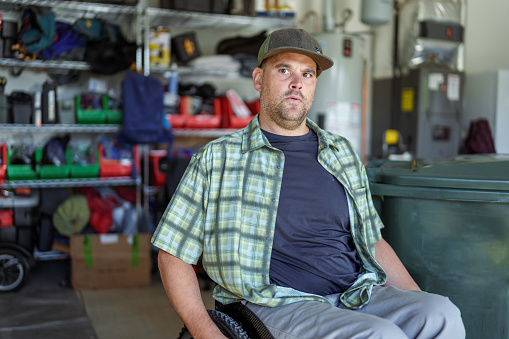 A Caucasian man with a physical disability who uses a wheelchair sits in his home garage looking directly at the camera.