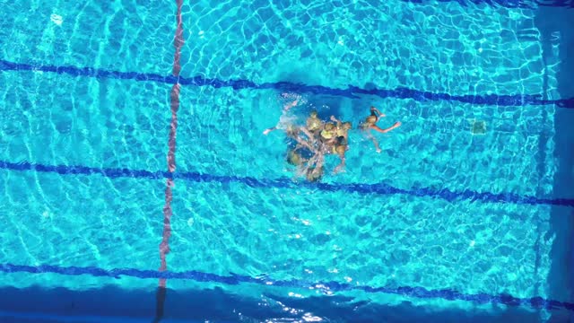 Aerial view of eight teenage girls learn figures in the pool. Girls learn competitive swimming in the pool. Team water sports. Synchronized swimming.