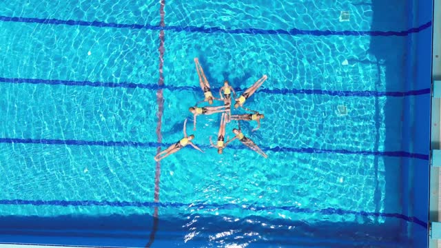 Aerial view of eight teenage girls learn figures in the pool. Girls learn competitive swimming in the pool. Team water sports. Synchronized swimming.