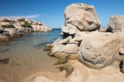 The wondrous and colorful waters of the Mediterranean sea on a summer day, in Valle dell'Erica beach near Santa Teresa Gallura. Some boulders carved by the strong wind sideline the beach.