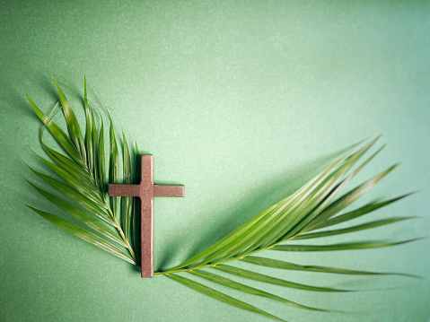 Lent Season,Holy Week and Palm Sunday concepts - closed up wooden cross with palm leaf in green background. Stock photo.