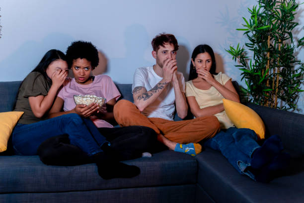 Friends Reacting to a Thrilling Movie Scene Friends on edge while watching a thrilling scene in a movie, with expressions of shock. suspenseful stock pictures, royalty-free photos & images