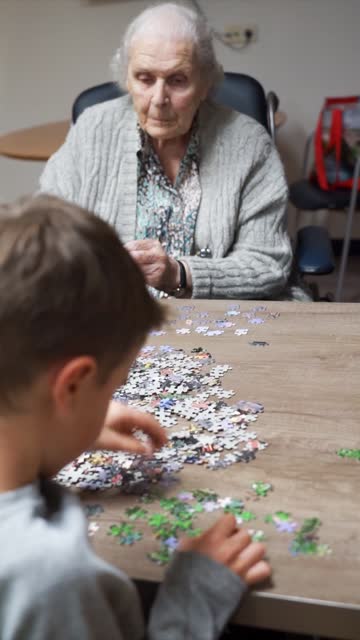 Boy playing with his great-grandmother to do a puzzle in a nursing home