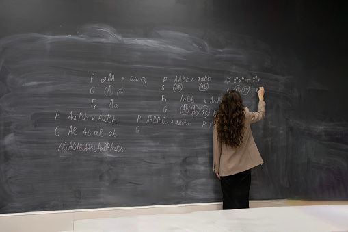 young smart female teacher in university writing biology formulas on the huge blackboard