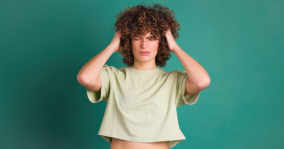 Adult woman with her hands on her head because of a confusion. Studio shot green background