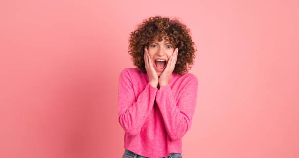 Stunned young woman standing with opened mouth on pink background stock photo