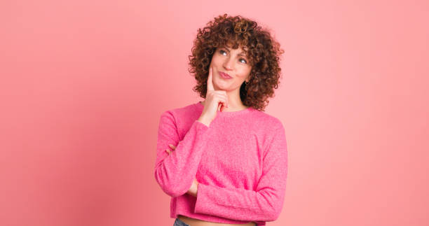 istock Thoughtful young woman touching face and smiling on pink background 1939396576