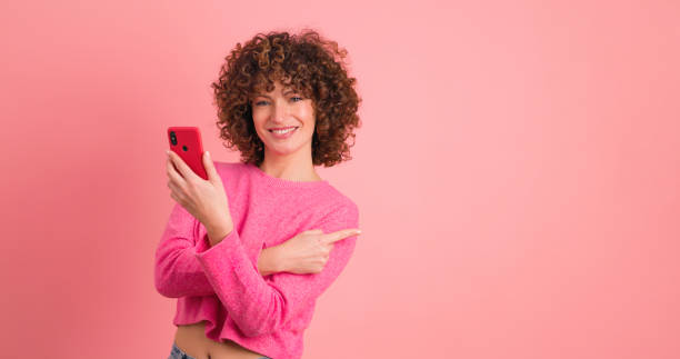 istock Young woman point to pink wall on pink background 1939398073