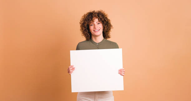 istock Happy woman holding blank paper in beige studio 1939406771
