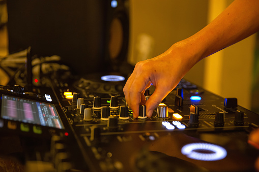 Close up shot unrecognizable hand of female dj holding a button to adjust the music tone.  concept: dj mixes the track at a party, playing music.