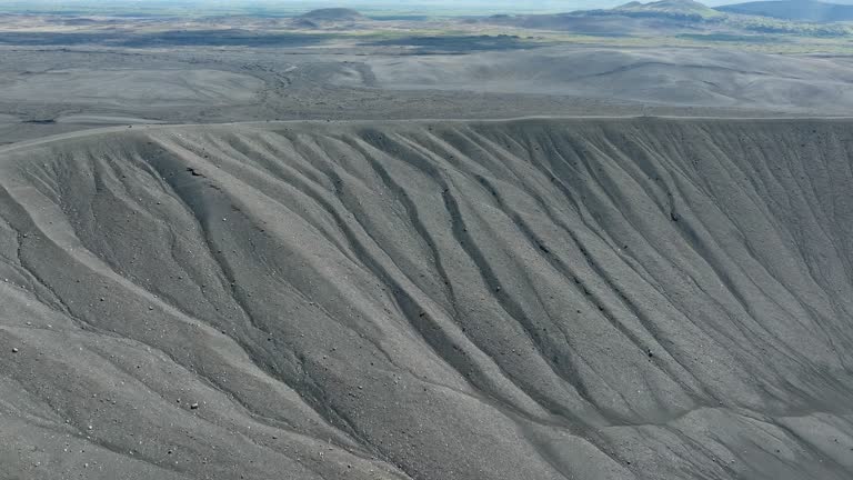 Volcano crater with black sand and scenic landscape in the background, aerial