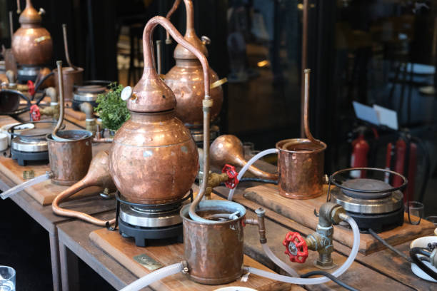 small copper stills and distilling equipment arranged on a decorated table. - distillation tower стоковые фото и изображения