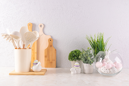 Easter holiday decorations on a light kitchen countertop with eco-friendly kitchen utensils and green plants in pots. Easter concept