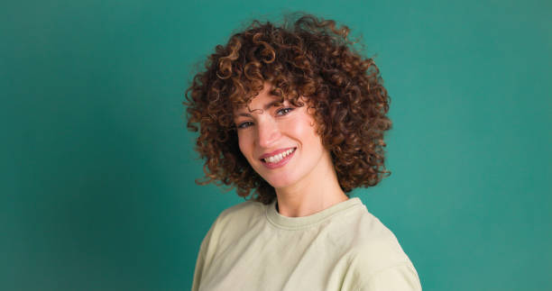 istock Smiling standing young curly haired woman on green background 1939496628