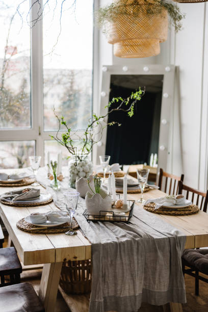 istock Interior design of easter dining room. Happy easter dinner with decor at home. Minimalist composition in living room with copy space, hanging lamp, candles, easter eggs, vase with twig, branch, leaves 1939500048