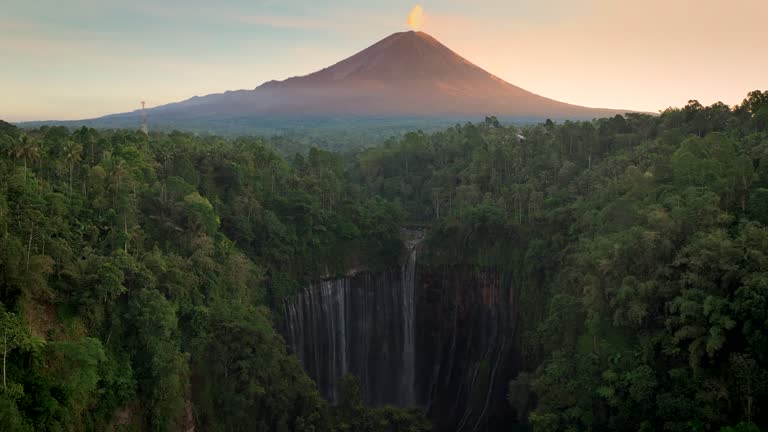 Scenic aerial view sunrise scene of Tumpak Sewu waterfall with Semeru Volcano Background with the jungles on Java Island, Indonesia