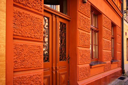 Facade of ancient building with orange wall, old wooden door and two windows. Torun, Poland, August 2023