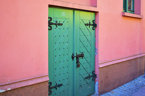 Old green door with ancient metal parts on the pink color facade. Historical architecture. Old street. Poland, Torun, August 2023.