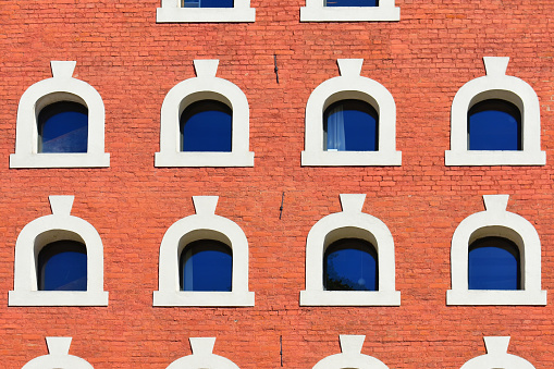 Facade of the historic building with small semicircular windows, white frames and a red brick wall. Ancient architecture. Torun, Poland, August 2023