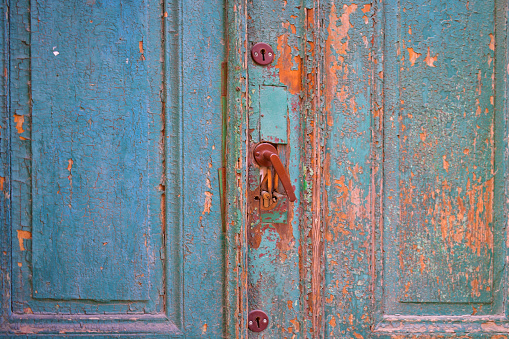 Old blue wooden door with cracks and fallen paint, with a metal handle and details. Grunge texture. Torun, Poland, August 2023