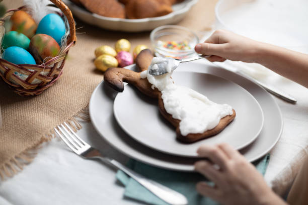 Childs hands decorating Easter bunny shaped cookie with icing on festive decorated table