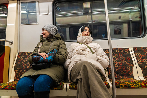 A happy mother and daughter smiling and enjoying a subway train ride together in the city. They are sitting comfortably and looking out the window, surrounded by urban scenery.