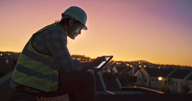 istock Construction worker man, tablet and roof at sunset, scroll or click for planning, development or urban expansion. Engineer, person and digital touchscreen for blueprint, sketch or discussion in city 1939502831