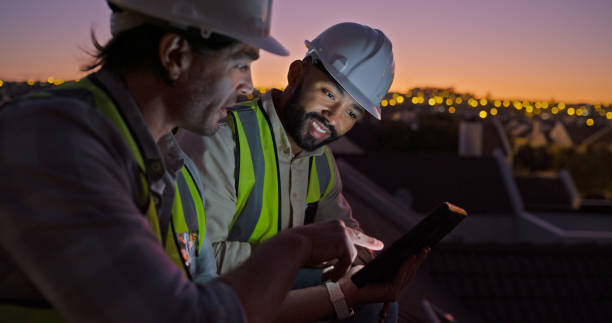istock Engineer men, tablet and roof at sunset, talking or click for planning, development or urban expansion. Construction worker, people and digital touchscreen for blueprint, sketch or discussion in city 1939502840