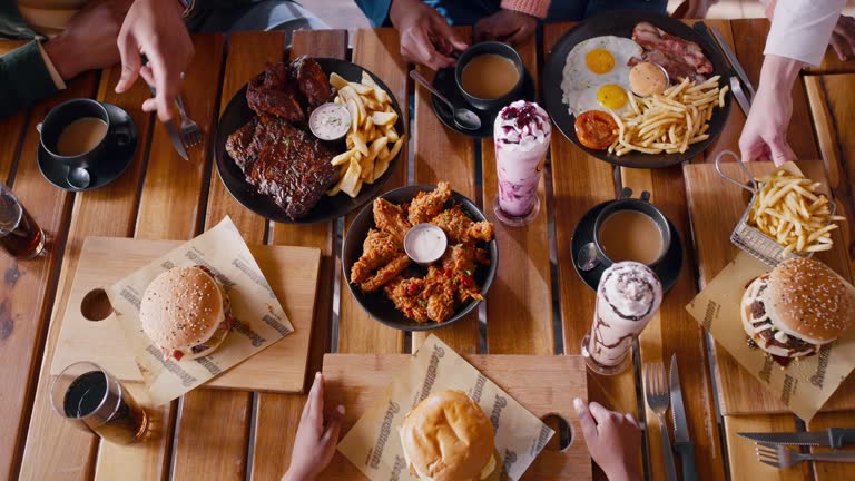 People, hands and food at restaurant for dining, eating or meal together above on table at indoor cafe. Top view of waiter serving customers or hungry family a burger and chips for dinner snack