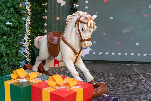 a white baby horse next to a Christmas tree and gift boxes. New Year decorations.