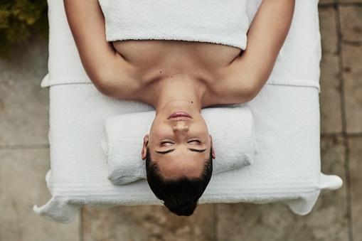 Woman, bed and relax at spa, above and peace with sleep for wellness, beauty or natural treatment. Girl, person or client on table for physical therapy, rest or recovery with healing in luxury salon