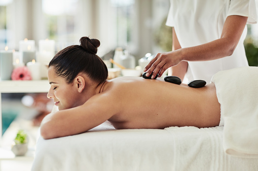 Spa, woman and hot stone with massage on back for physical therapy, wellness and aromatherapy with relax. Masseuse, luxury service or body care for peace, stress relief and skincare in hotel with zen