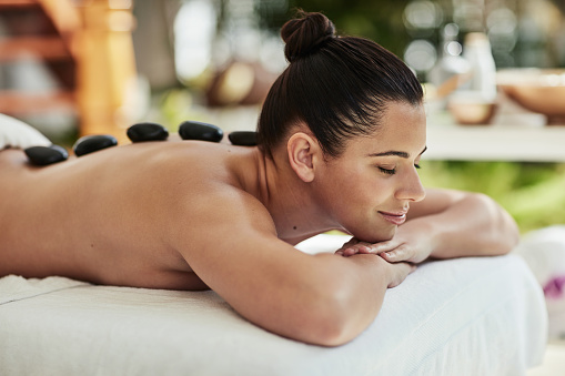Woman, spa and happy with hot stone on bed, peace or smile for thinking, natural treatment or sleep. Girl, person and relax for wellness, health and salon with rock massage, spine or physical therapy