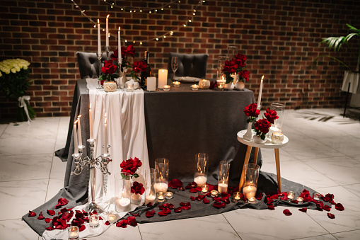 Location for surprise proposal at night. Luxury romantic date.  Decoration, flower petals, burning candles. Table setting in restaurant for the event. Candlelight for couple on Valentine's day.