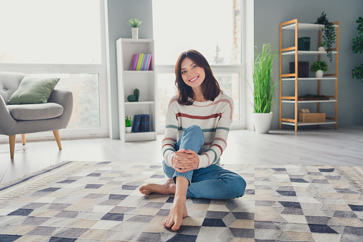 Full length portrait of pretty cheerful peaceful person sit carpet floor good mood weekend calmness apartment inside.