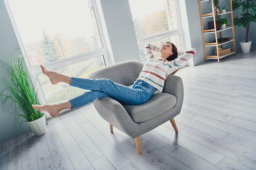 Full size portrait of peaceful cheerful girl sit comfy chair barefoot hands behind head weekend morning chill house inside.