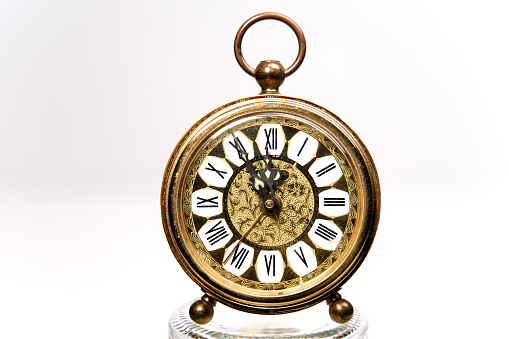 an old golden analog alarm clock with mechanical movement isolated on colored background