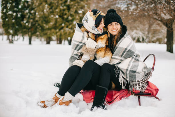 Two person sledding on an orange plastic sled down a snowy hill with bare trees in the background