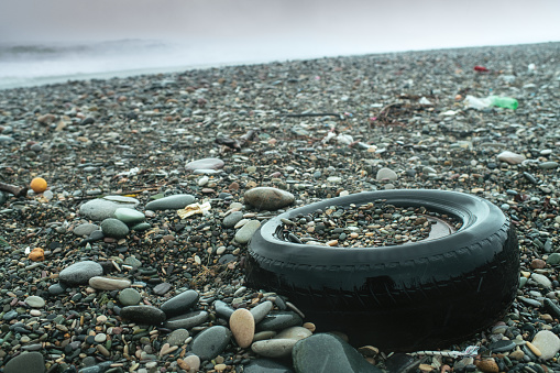 Old car tire on the beach. Plastic pollution and ecological problems concept.