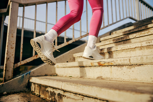 Female runner's legs running up the staircase in urban exterior.