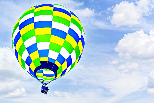 Colorful hot air balloon flying over blue sky with white clouds